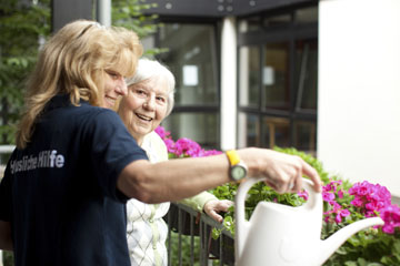 Foto: Pflegekraft hilft Seniorin beim Blumengieen