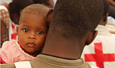 Menschlichkeit: Baby schaut ber Schulter eines Rotkreuzhelfers